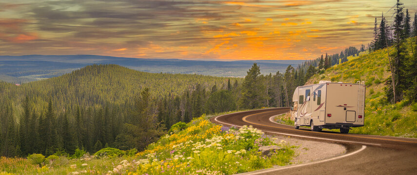 Camper Driving Down Road in The Beautiful Countryside Among Pine Trees and Flowers.