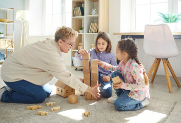 Happy grandmother playing with grandchildren using toys on the floor during leisure time at home, focusing on family playtime and relaxation with bonding and joyful shared experiences.
