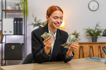 Young businesswoman at home office counts dollars grinning at rising earnings and secure future. Freelancer girl at table stacks money celebrating salary bonus great financial victory investment dream