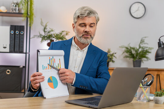 Middle-aged businessman at home office shows chart on laptop in remote call pointing at big drop. Freelancer guy at table proposes recovery plan gestures confident explaining steps for future growth. - Powered by Adobe