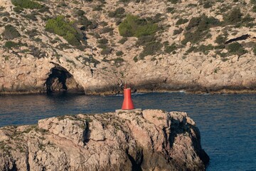 Red Navigation Beacon on Rocky Coast with Sea Cave
