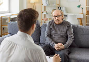 Depressed balding senior older adult man in glasses having therapy session appointment with young...