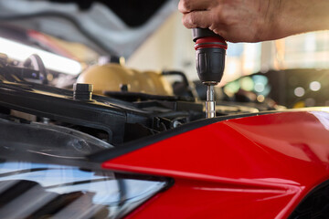 Mechanic repairs vehicle, Precision automotive work under vehicle with tools and focus, Detailed shot of technician tightening bumper beneath car in workshop environment