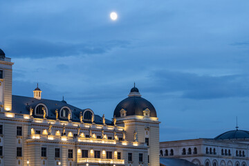 opulent building with golden illumination under an intense blue twilight sky and a bright moon; elegant neoclassical architecture