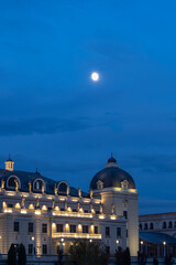 imposing building with baroque-neoclassical architecture illuminated at dusk or night, with a full moon in the dark blue sky, providing a dramatic, elegant, and mysterious atmosphere