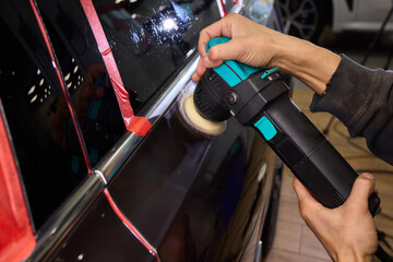 Polishing black car surface thoroughly, Detailed buffing to achieve showroom quality shine, Expert technician uses orbital buffer and foam pad to enhance vehicle gloss