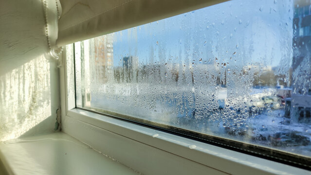 Drops of condensation on a poor-quality PVC window. Foggy glass, ice-covered, water on the windowsill