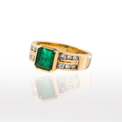 Yellow gold ring with emerald and brilliant-cut diamonds photographed on a white background with reflection