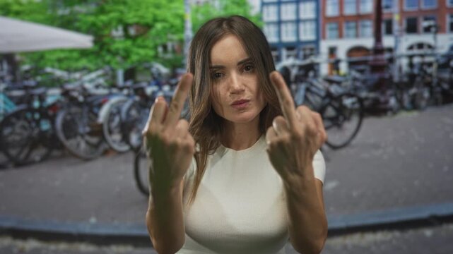 Young hispanic woman in white t-shirt flips middle fingers with bare hands on city street; anger defiance.