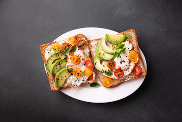 Tasty homemade toast for breakfast with fried eggs, cream cheese, avocado, cherry tomatoes and...