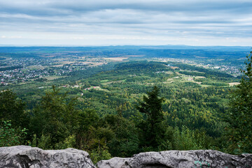 Panoramic view of a lush green forest and a village in a valley, with a cloudy sky above, from the top of a mountain.