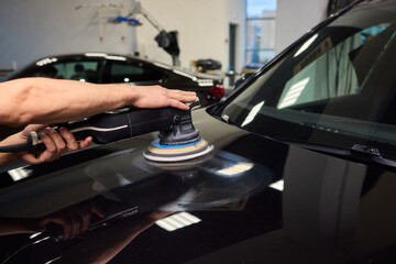 Polishing black car surface thoroughly, Detailed buffing to achieve showroom quality shine, Expert technician uses orbital buffer and foam pad to enhance vehicle gloss