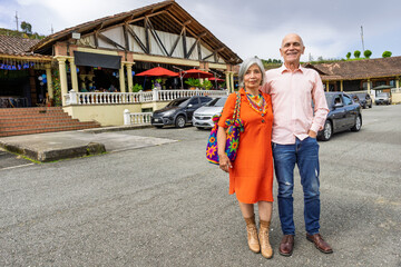 Colombian senior couple posing in front of rustic restaurant during outing in Guarne, Antioquia.