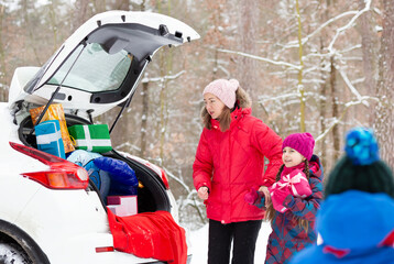 Smiling mom with her kids surrounded by holiday gift boxes in back of snowy car, enjoying magical winter forest day. Merry Christmas