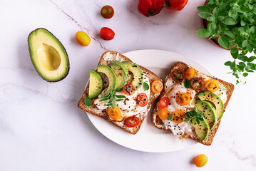 Tasty homemade toasts for breakfast with fried eggs, cream cheese, avocado, cherry tomatoes and...