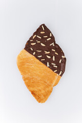 Flaky croissant half dipped in dark chocolate with almond slices on white background