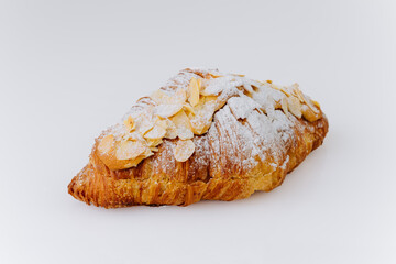 Almond croissant topped with powdered sugar and sliced nuts on white background, French pastry