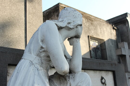 Primer plano de estatua de m&aacute;rmol de mujer en duelo con la mano en la frente, expresi&oacute;n de tristeza, dolor y luto en cementerio antiguo, arte funerario
