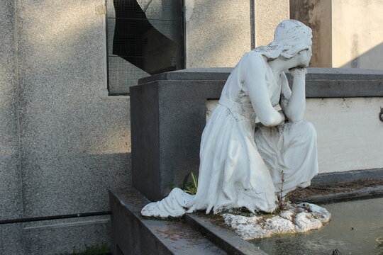 Escultura de mujer de rodillas en actitud de luto y tristeza sobre l&aacute;pida o mausoleo antiguo, s&iacute;mbolo de duelo, recuerdo y arte funerario en cementerio