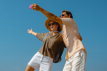 Happy caucasian couple taking selfie at the beach under clear blue sky