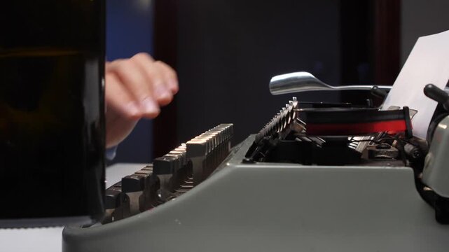 Writers hands typing keys on an old retro manual typewriter with a dark beer or alcohol bottle resting nearby, symbolizing inspiration or writer's block