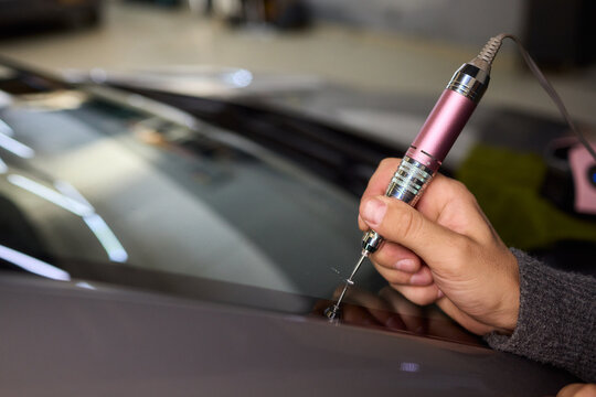 Glass repair process, Detailed shot of resin filling windshield flaw, Focuses on craftsman meticulously repairing starshaped chip on car windshield using adhesive syringe