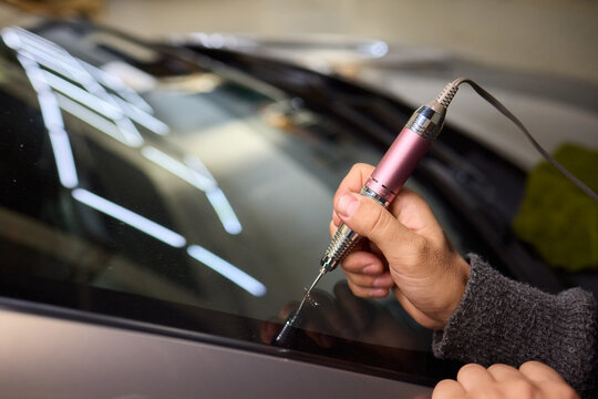 Glass repair process, Detailed shot of resin filling windshield flaw, Focuses on craftsman meticulously repairing starshaped chip on car windshield using adhesive syringe
