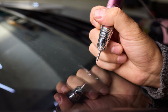 Glass repair process, Detailed shot of resin filling windshield flaw, Focuses on craftsman meticulously repairing starshaped chip on car windshield using adhesive syringe