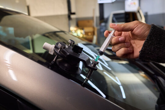Technician carefully aligns syringe to ensure proper resin flow and adhesion, Clear focus on precise positioning of injector for effective windshield resin repair process