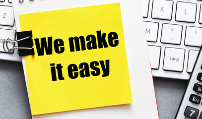 WE MAKE IT EASY words written on a yellow piece of paper on the desk. Concept for business.