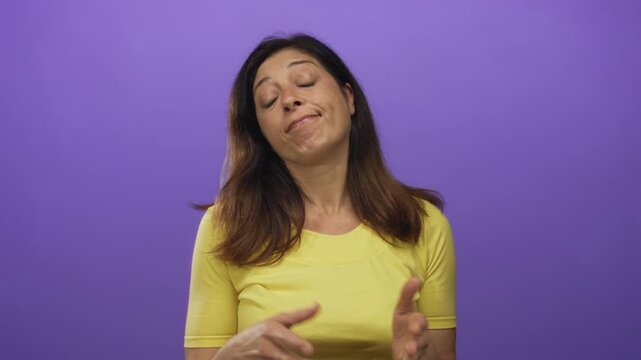Middle age hispanic woman shrugging shoulders with eyes closed against a vibrant purple studio background wearing a yellow top; indifference.