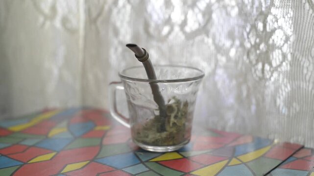 Preparando el mate, vertiendo la yerba con una cuchara, sobre la mesa, al lado de la ventana