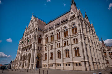 Fototapeta premium Budapest, Hungary - July 27, 2025: The Hungarian Parliament Building viewed from its garden side, showcasing its magnificent Neo-Gothic architecture with detailed spires and ornate stonework.