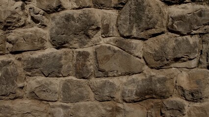 A natural, rugged, aged brown and gray dry stone or concrete retaining wall texture background, featuring an irregular rock pattern and small green ivy climbing plant on the side.