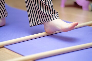 Teen girl's foot performing therapeutic gymnastics with a wooden pole on a blue exercise mat