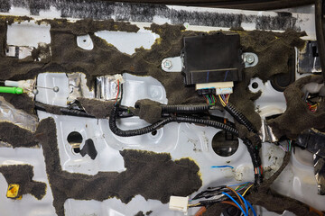 Corroded metal and broken parts, Rust stained door with shredded insulation material, Damaged automobile interior showcasing rusted surfaces and frayed insulation layers