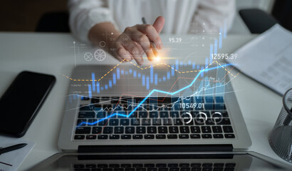 A business professional reviews financial data on a laptop, with a digital graph illustrating stock...