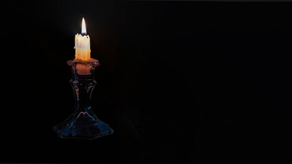 Close up of a burning candle on black background with huge copy space right side. Horizontal image.