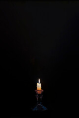 Close up of a burning candle on black background with huge copy space on top.. Vertical image.