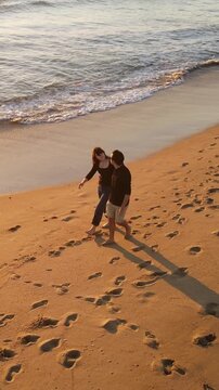 Aerial shot of a happy couple walking on the beach at sunset in Southern California. Vertical Video.