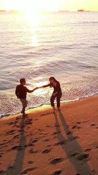 Aerial shot of a happy couple walking on the beach at sunset in Southern California. Vertical Video.