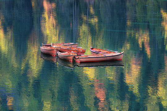 Red wooden boats in calm lake. The silhouette is reflecting on the water. Location place Lake Braies, Dolomites, Italy, Europe.