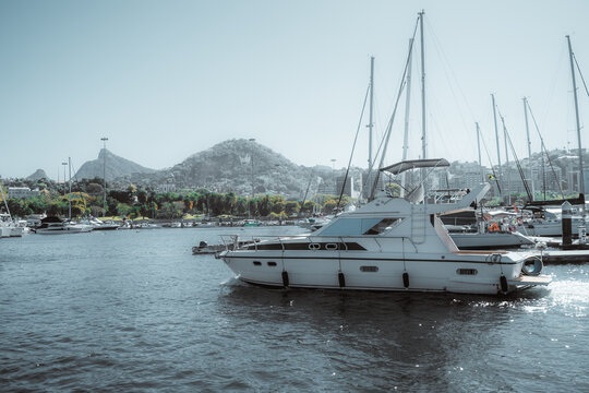 Luxury motor yacht docked at marina in Rio de Janeiro, Brazil, surrounded by sailboats and tropical hills under bright summer light, showcasing nautical lifestyle and leisure travel - Powered by Adobe