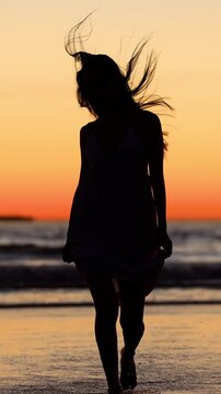 Attractive Asian woman enjoys a walk on the beach at sunset in Southern California. Slow Motion. Vertical Video.