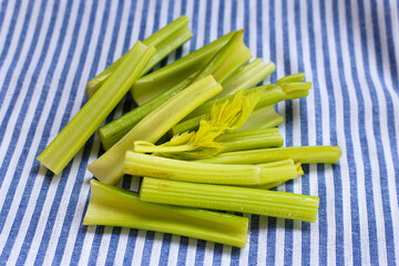 Fresh celery stalks cut into short pieces on a striped cloth.