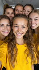 Obraz premium A group of seven happy young women, all in matching yellow shirts, smile directly at the camera in what appears to be a group selfie indoors