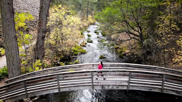 Aerial shot of a Asian female hiker walking across a bridge over Burney Creek in Northern California.
