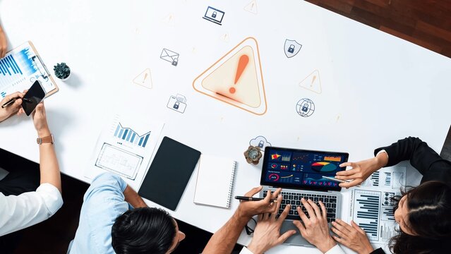 A business team actively collaborates in a modern office, analyzing data and discussing risk management with a laptop and various charts displayed on the table. Raster - Powered by Adobe