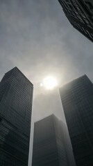 Urban skyscrapers rise against a hazy sky, sun visible