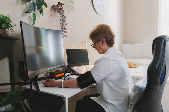 An elderly woman measures her blood pressure in her home office.